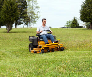 Senior retired male cutting the grass on expansive lawn using yellow zero-turn mower