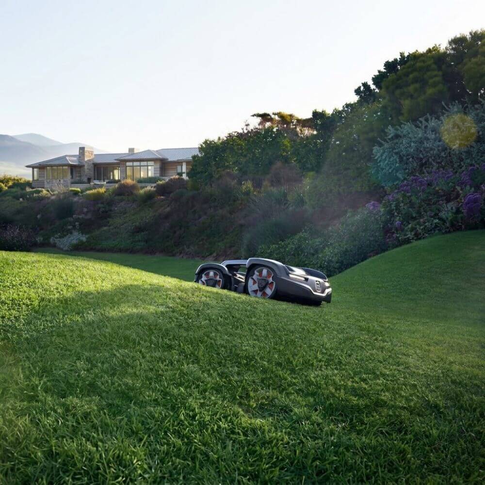 Husqvarna Automower 435 iQ AWD robotic mower actively mowing a steep sloped residential lawn in New Hampshire showing all-wheel drive traction on grade