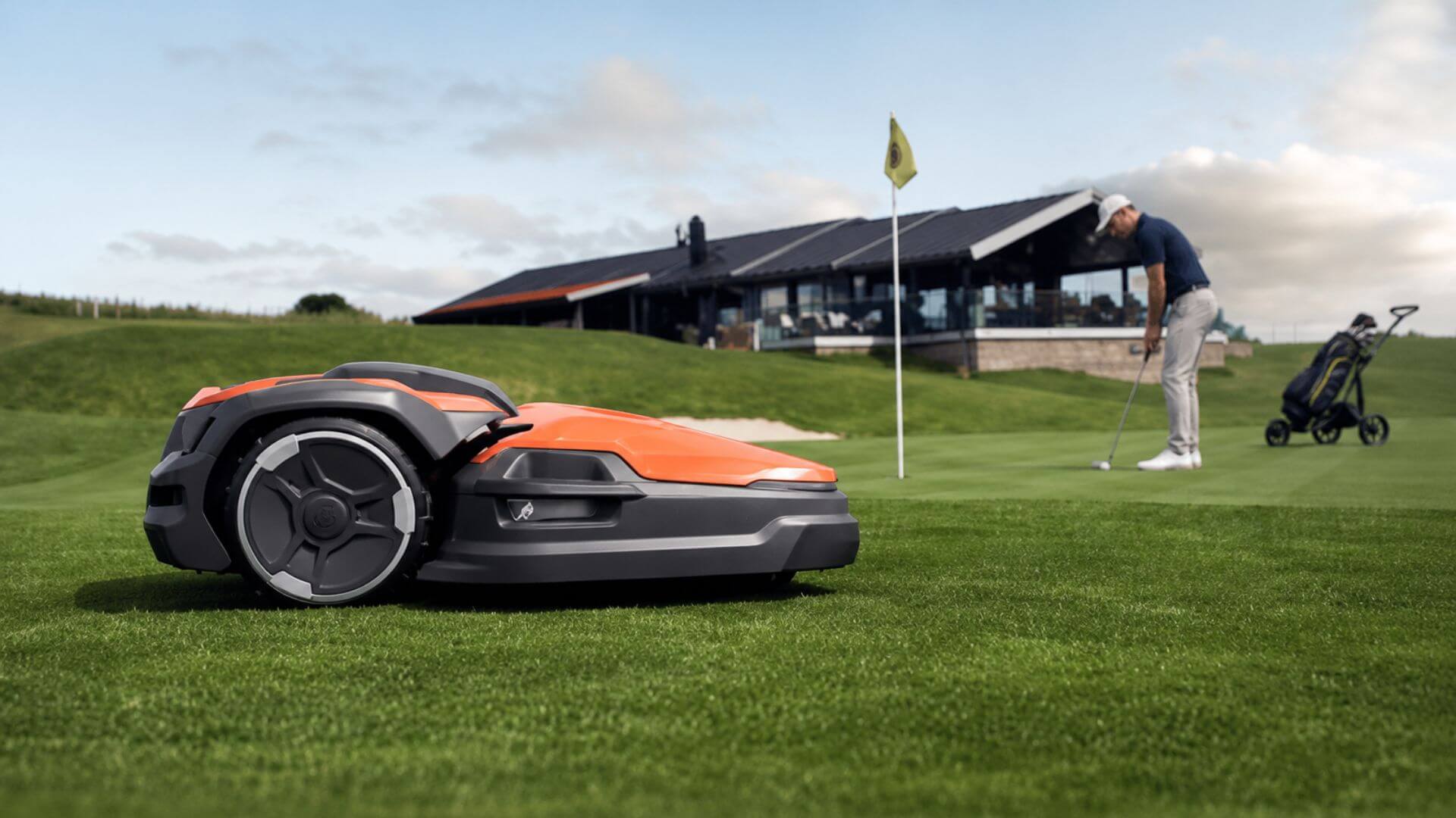 Husqvarna robotic mower operating on a golf course near a putting green while a golfer lines up a putt.