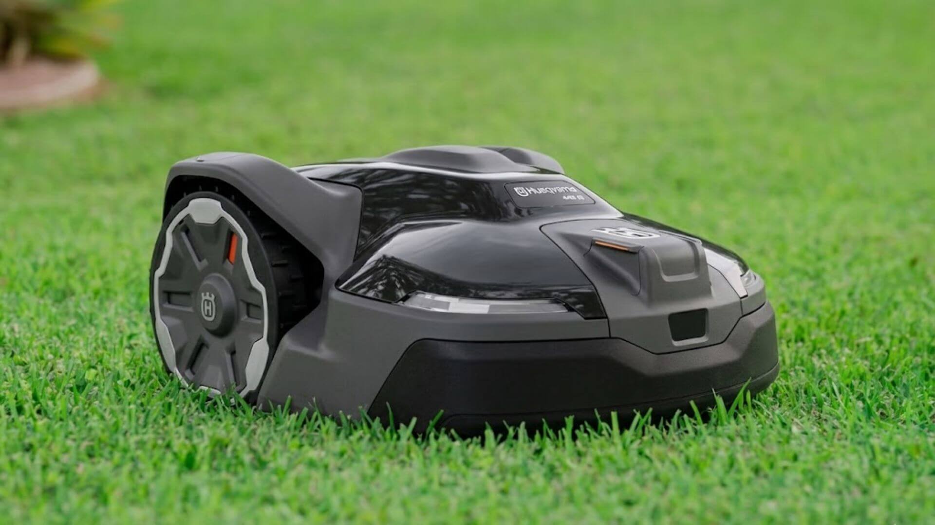 Close-up of a Husqvarna Automower 440iQ robotic mower cutting healthy green grass in a residential yard. 